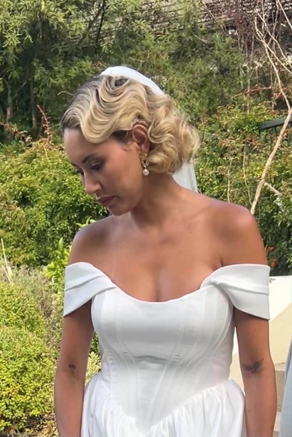 Vintage-inspired finger-wave updo with cathedral veil, bride looking down in a garden setting